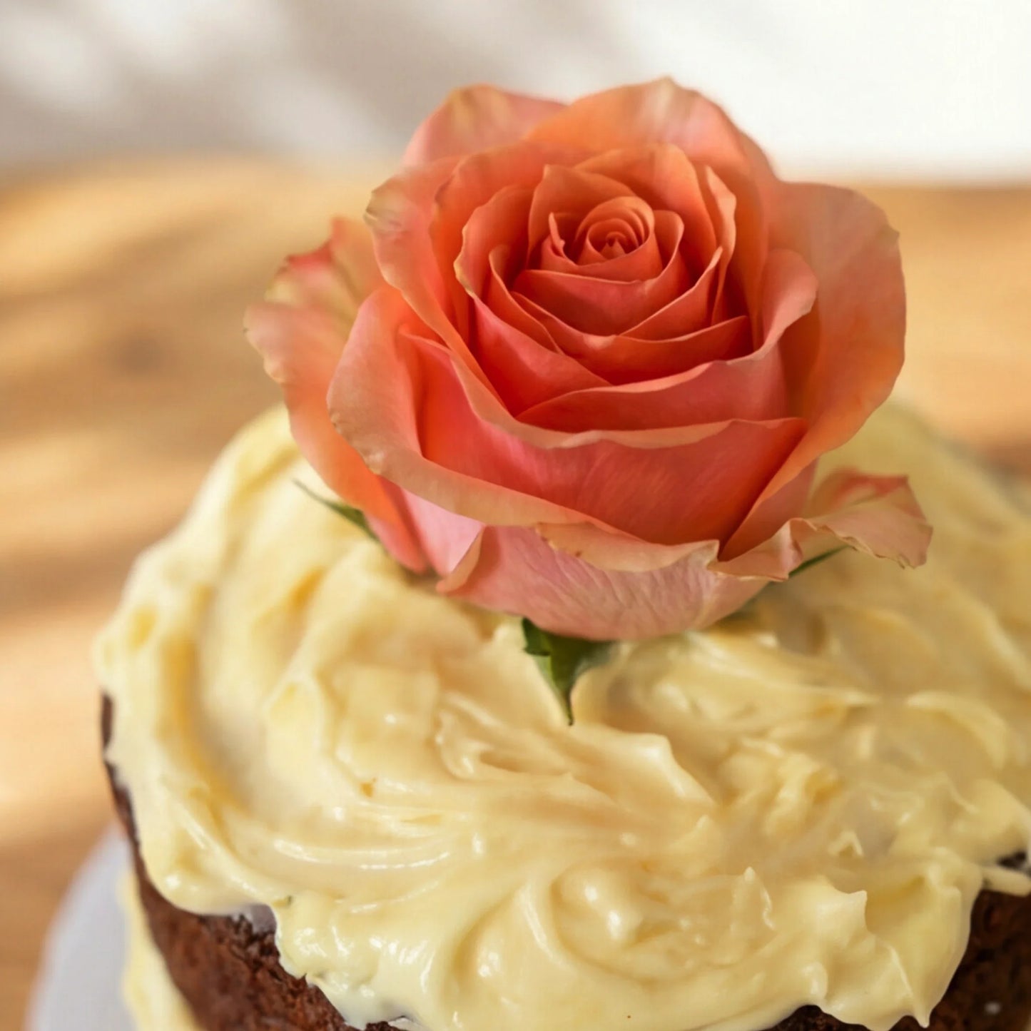 Close-up of the fresh coral rose crowning the cream cheese frosting on Carrot Cake in Bloom carrot cake