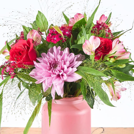 Cherry Bombshell - Flower Guy shows a lush mix of red roses, pink blooms, and greenery bursting from a pink ceramic jar.
