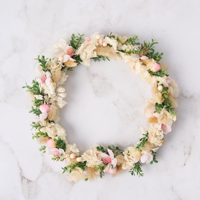 A soft pastel floral crown with cream and pink flowers, lush greenery, perfect for weddings or special occasions.