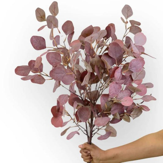 A hand holding a large bouquet of Eucalyptus Light Burgundy artificial foliage, highlighting the rich blend of light burgundy leaves in a full, realistic arrangement.