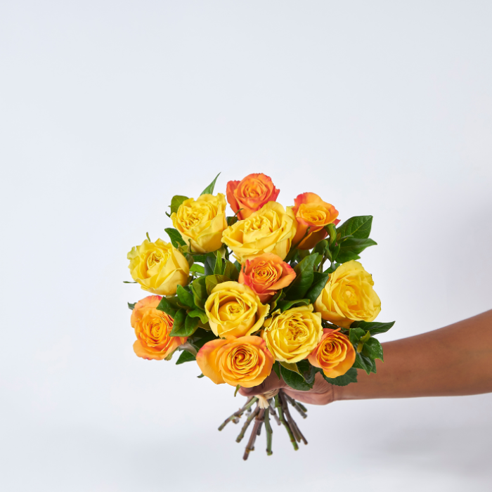 Hand-tied bouquet of vibrant yellow and orange roses with green foliage, wrapped in kraft paper, from Flower Guy