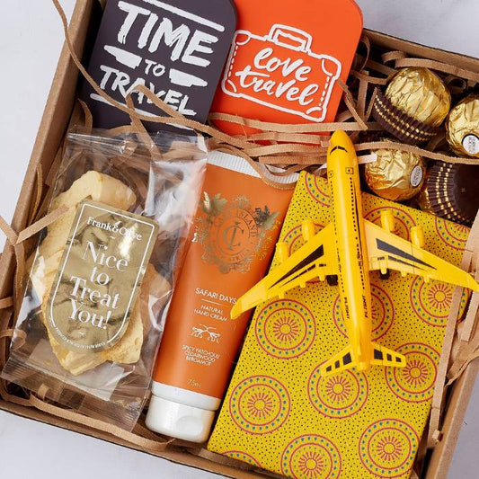 Close-up of Travel-Inspired Gift Box with colourful luggage tags, hand cream, golden chocolates, biscuit crisps, and yellow travel notebook.