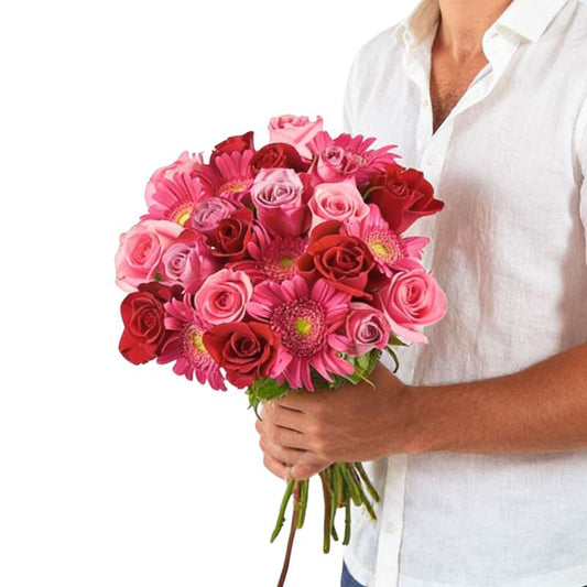 Love Actually bouquet close-up—hand holding red, magenta and pink roses with gerberas, wrapped in kraft paper | Flower Guy