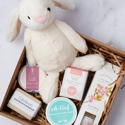 Close-up of Pamper Bunny for Babygirl featuring a cuddly bunny, balm, soy candle, cleansing bar, and shower steamer in a gift box.