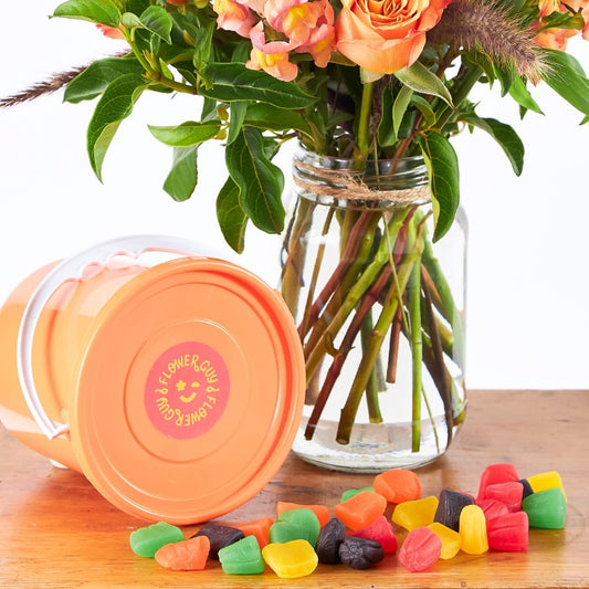 Peach Please! - Flower Guy features peach-toned blooms in a jar with a tipped orange tub and scattered jelly sweets on wooden surface.