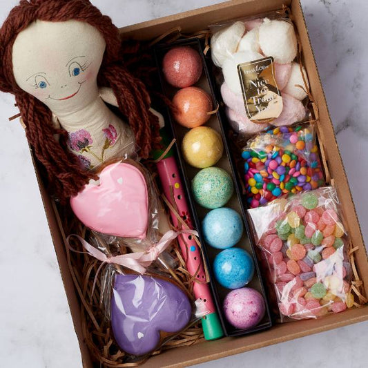 Close-up on the Rainbow Dreams gift box by Flower Guy featuring a handmade doll, heart-shaped cookies, bath bombs, and colourful sweets."