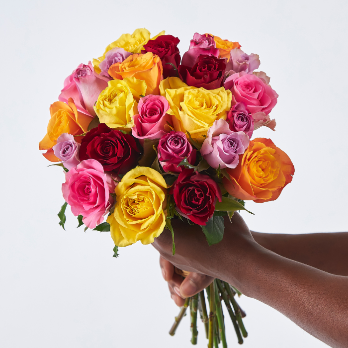 Close-up of hand-tied bouquet featuring multicoloured roses in yellow, orange, red, pink, and lilac tones, held in two hands
