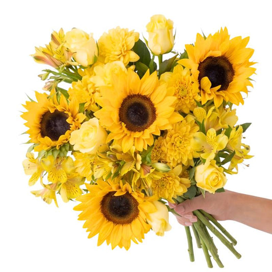 Close-up of the Sunstruck bouquet showing a bright sunflower head, yellow rose and soft yellow chrysanthemums nestled in green foliage.