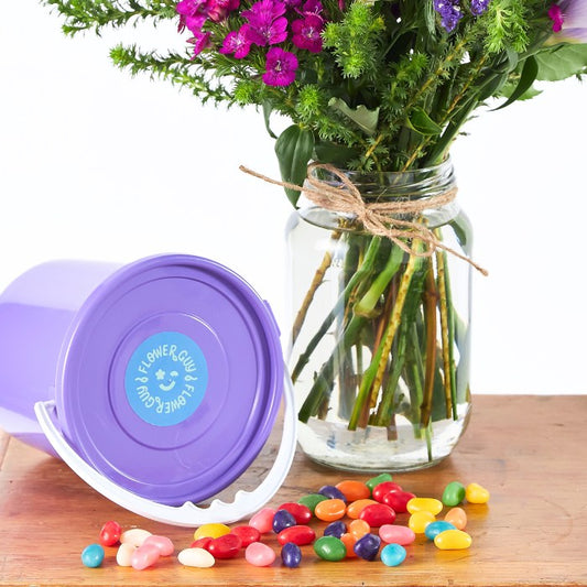 Sweet Talker - Flower Guy shows a colourful jar flower arrangement next to a purple tub and scattered jelly beans on a wooden table.