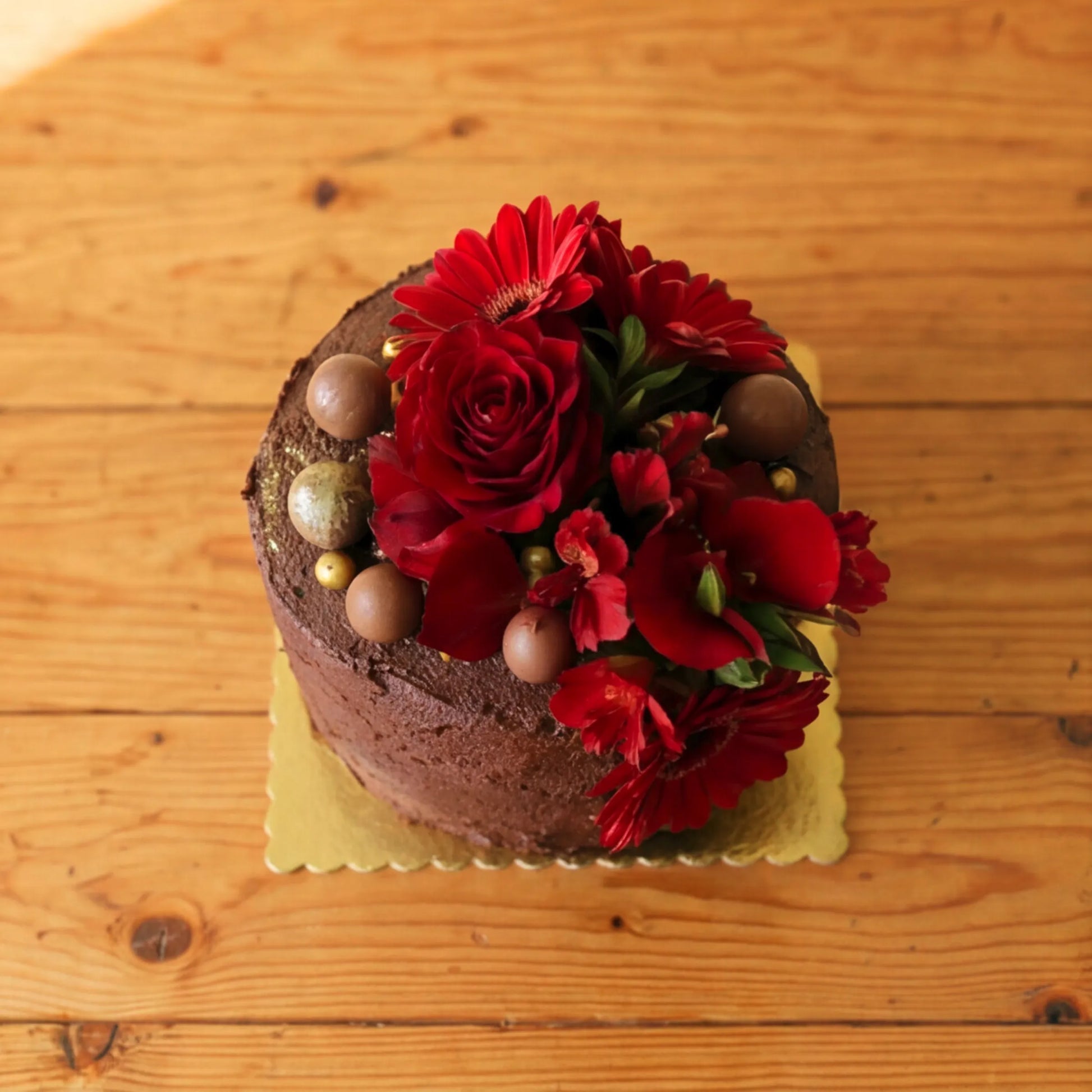 Overhead view of a Flower Guy chocolate celebration cake showing the floral crown of red roses, red gerbera daisies and chocolate truffles with gold edible pearls
