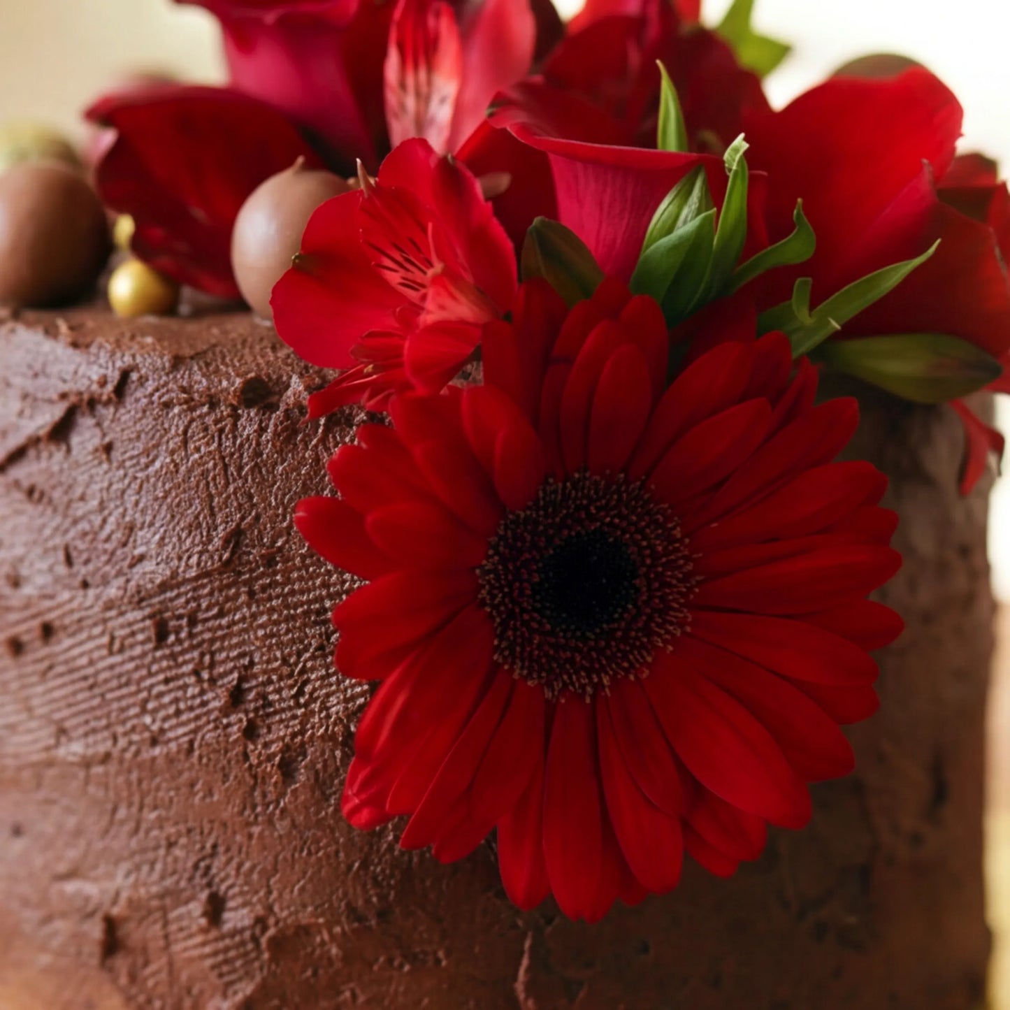 Macro shot of the fresh red gerbera daisy, red rose and red alstroemeria florals crowning the Flower Guy chocolate ganache celebration cake
