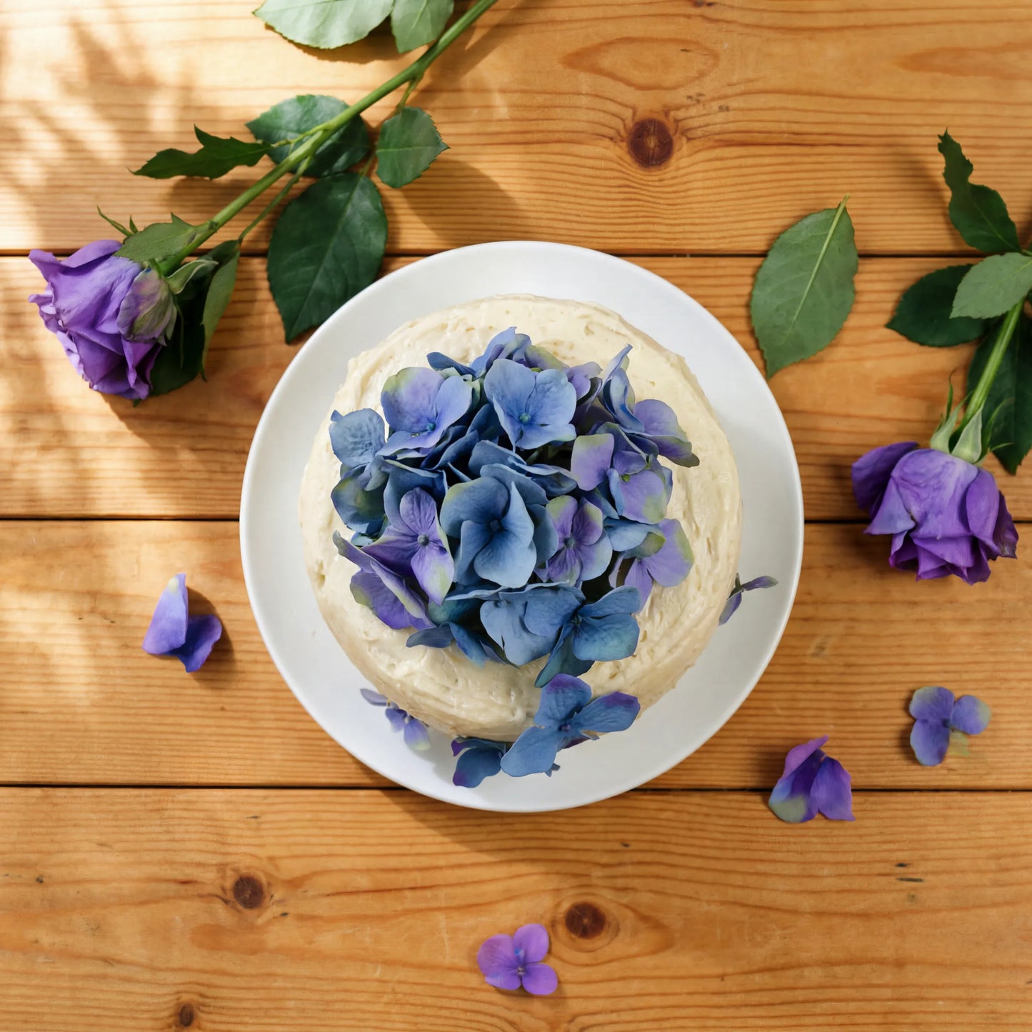 Overhead view of Blue Blossom Harmony Madeira Cake with blue hydrangea top and purple rose styling