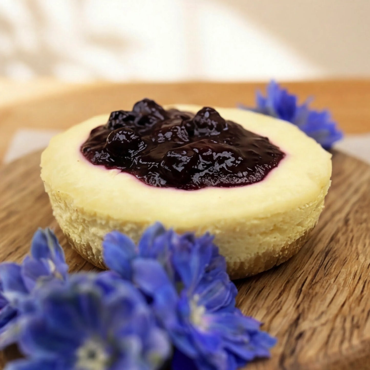 Macro close-up of Blueberry Cheesecake with glossy blueberry compote and fresh blue delphinium blooms