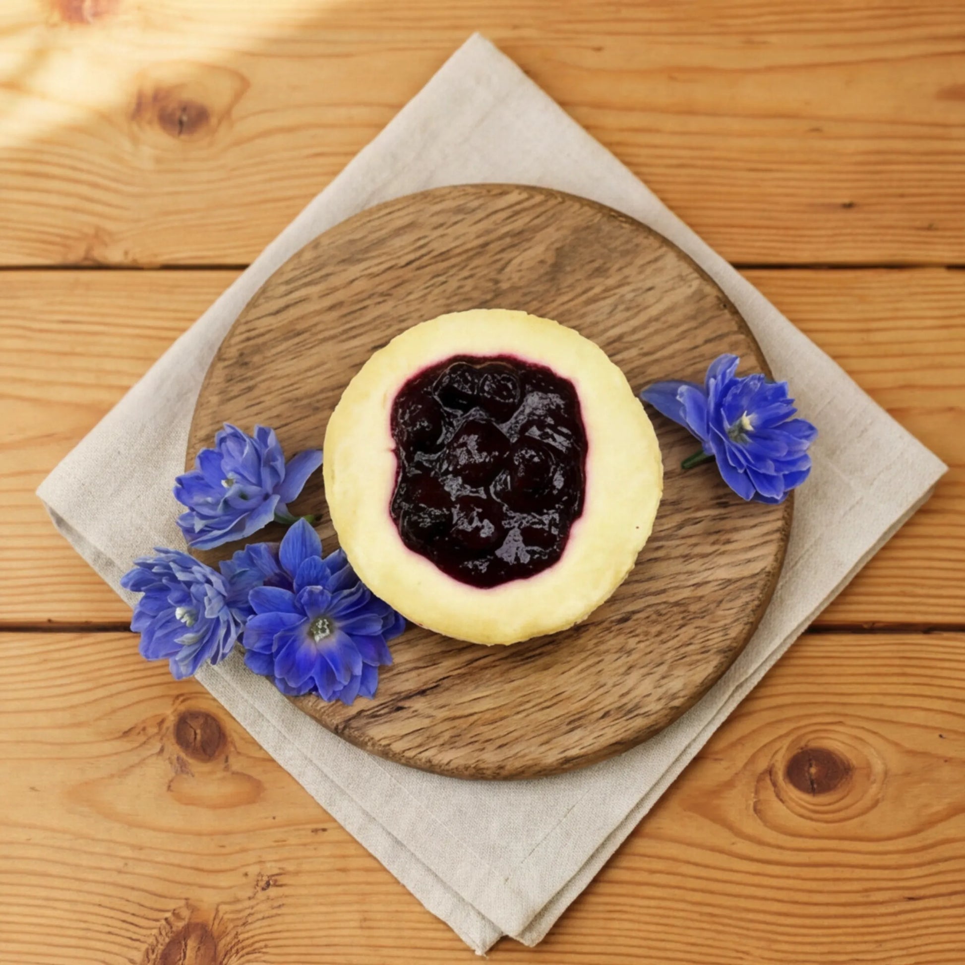 Overhead view of Blueberry Cheesecake with blue delphinium blooms styled on a round wooden board