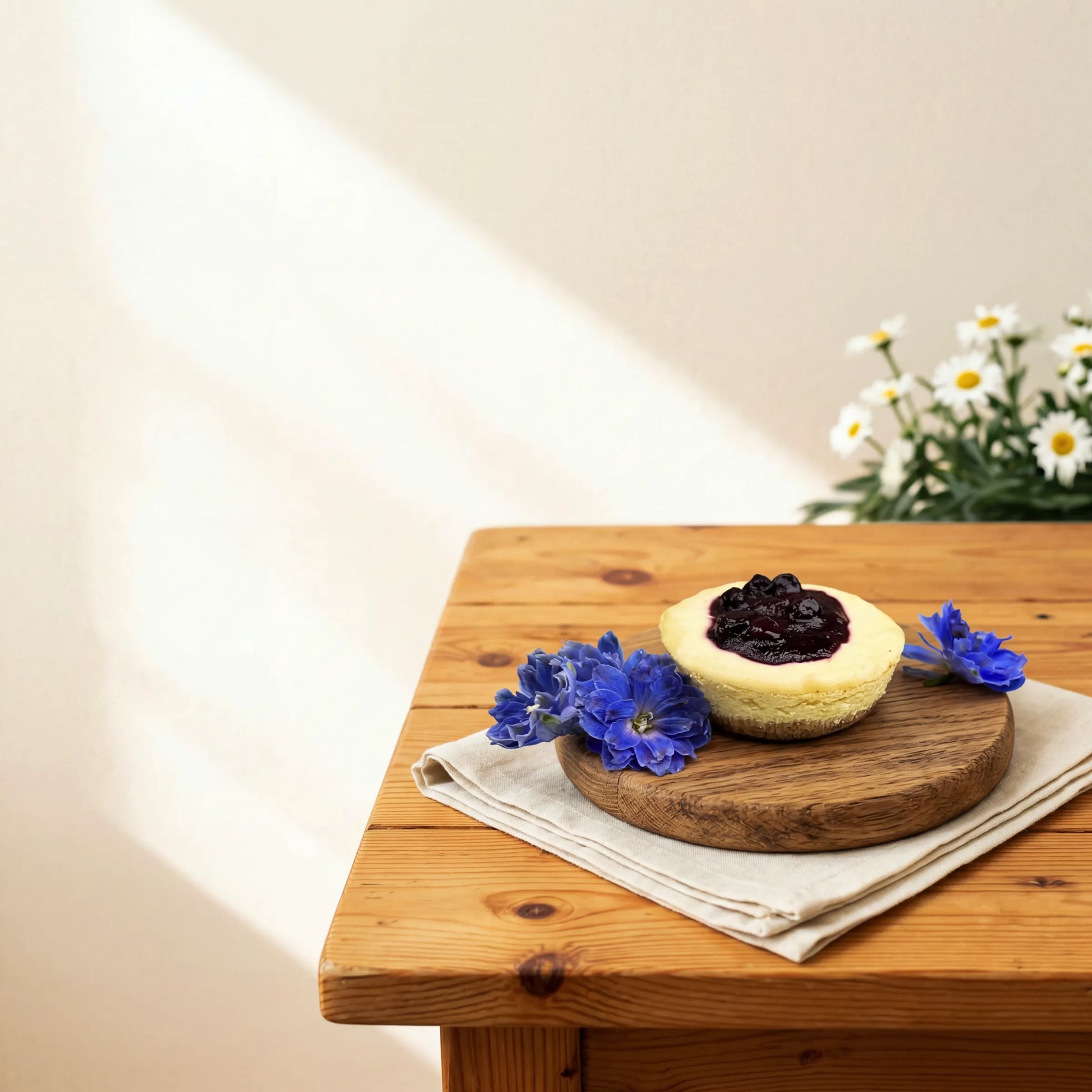 Blueberry Cheesecake on a serving board with blue delphinium and white daisies by Flower Guy