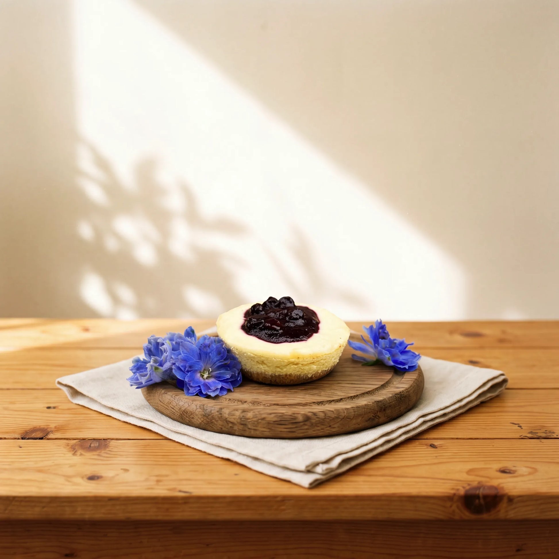 Front view of Blueberry Cheesecake with blueberry compote crown and blue delphinium florals by Flower Guy