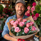 12 pink roses wrapped in kraft paper held by a flower delivery man wearing a cap | Flower Guy