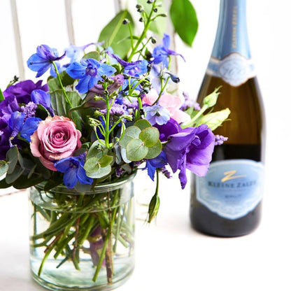 Bubbles and Pink—pink flower arrangement in a small glass vase with celebratory bubbly bottle in the background | Flower Guy