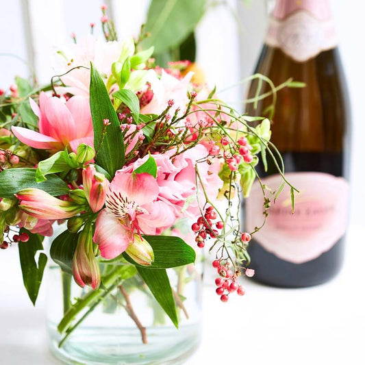 Bubbles and Pink—pink flower arrangement in a small glass vase with celebratory bubbly bottle in the background | Flower Guy