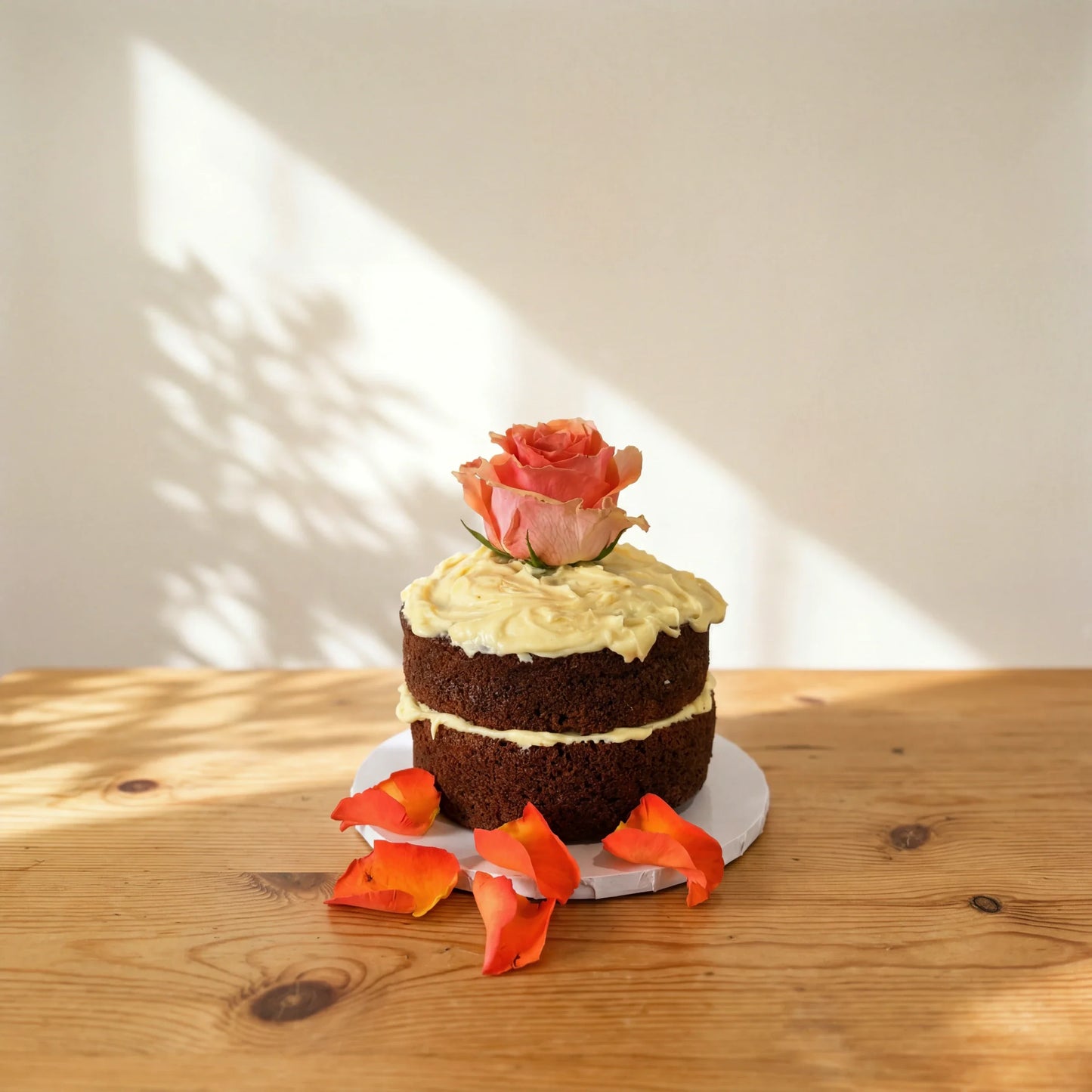 Carrot Cake in Bloom, a two-layer carrot cake with cream cheese frosting and a fresh rose, petals on the board
