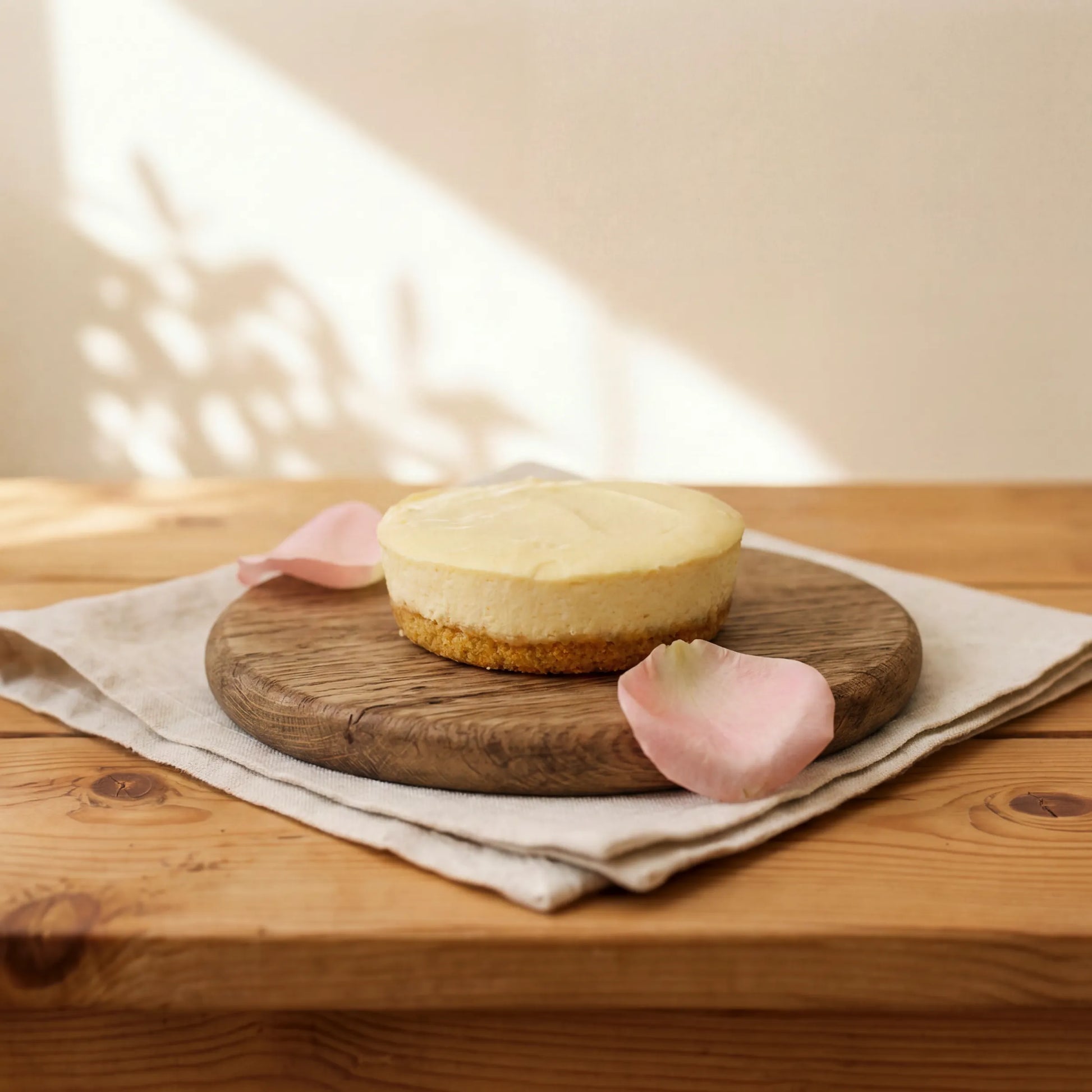 Lemon Cheesecake on oak board with pink rose petals and linen, by Flower Guy Cape Town