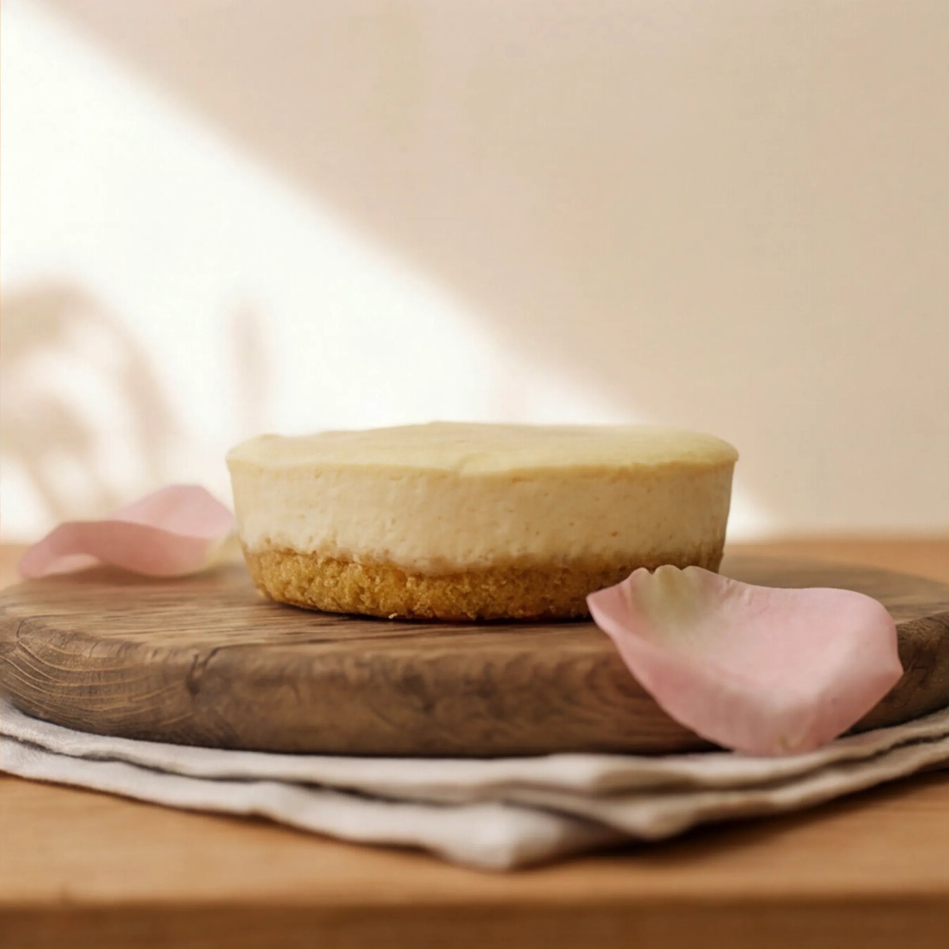 Side view of single-portion Lemon Cheesecake with golden biscuit base on oak board by Flower Guy