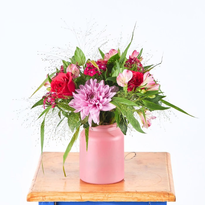 Cherry Bombshell - Flower Guy features a bold red and pink flower arrangement in a soft pink ceramic jar on a wooden table.