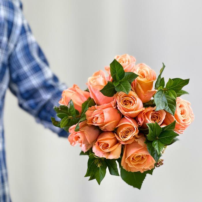 Man holding Hand-tied Coral Charm Rose Bouquet with 12 coral roses - Flower Guy