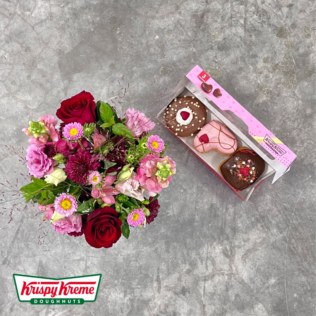 Elegant vase with pink lisianthus and red roses beside Krispy Kreme doughnuts box by Flower Guy