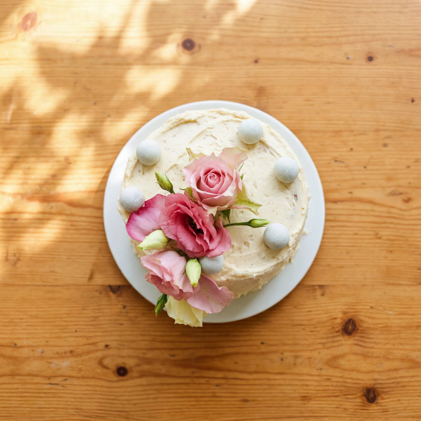 Overhead view of Garden Tea Party Cake topped with pink rose, lisianthus blooms and dove-grey chocolate pearls