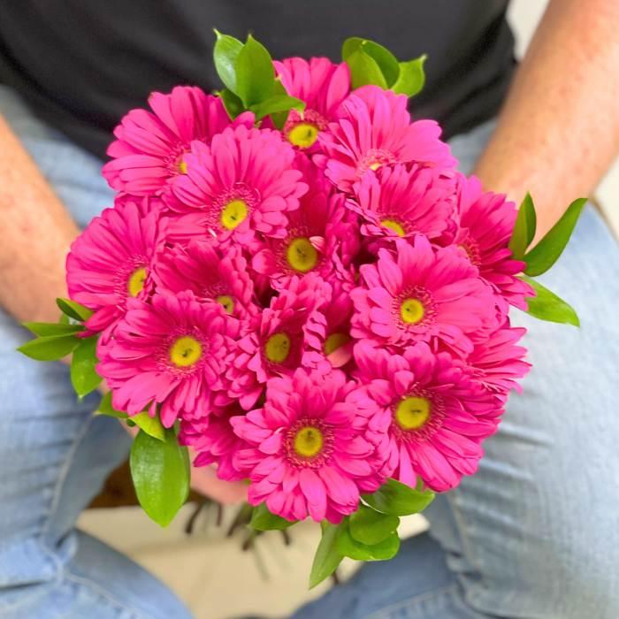 Flower Guy holding bouquet. Close-up view of pink Gerbera Glee Bouquet with greenery
