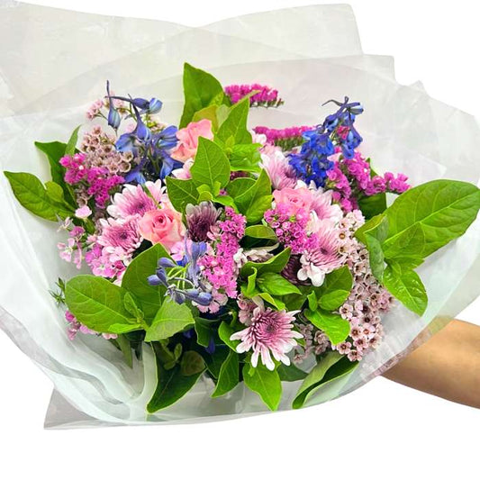 Jump for Joy Bouquet—hand holding pastel mixed flowers in pink and purple with lush greenery, wrapped gift-ready | Flower Guy