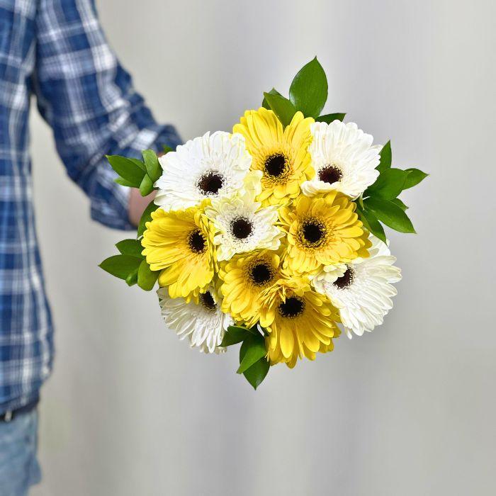 Man holding bright yellow and pristine white gerberas in a bouquet with greenery - Flower Guy