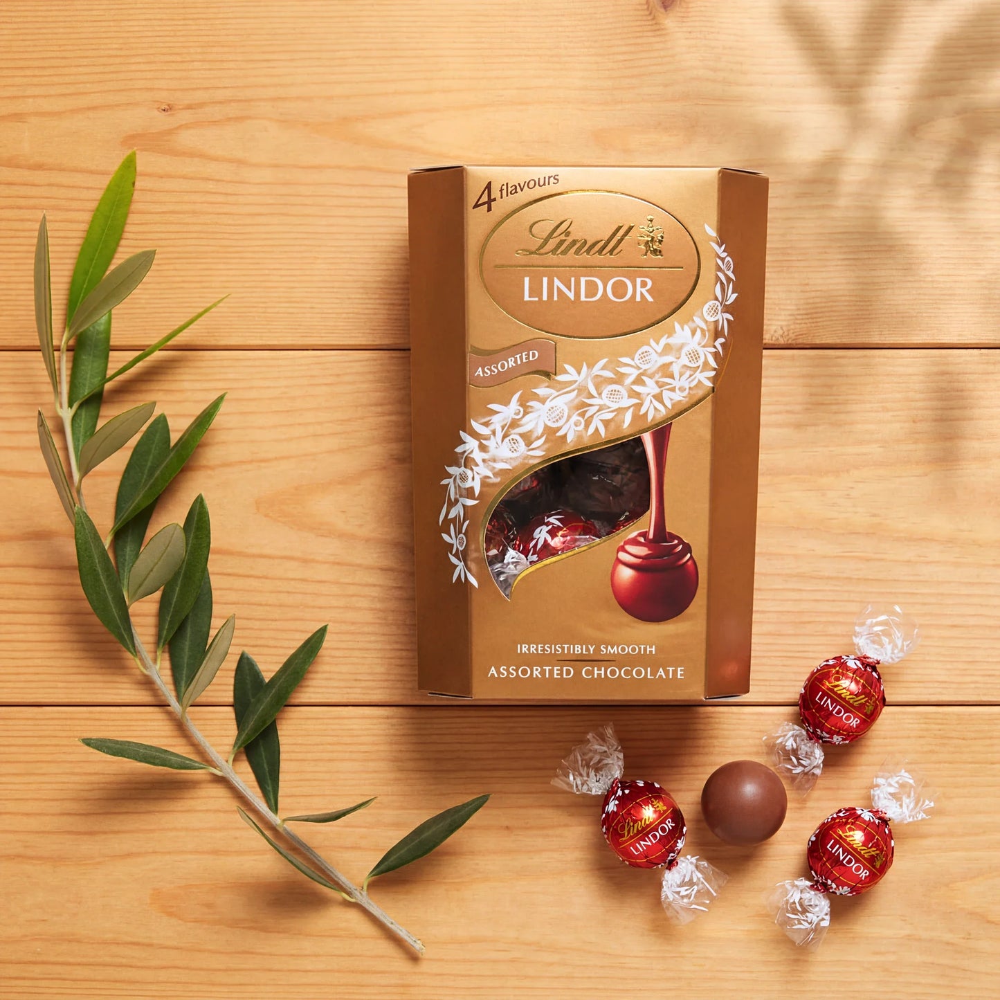 Flat lay of Lindt Lindor Assorted chocolate truffles and the gold 4-flavour box with an olive branch on wood