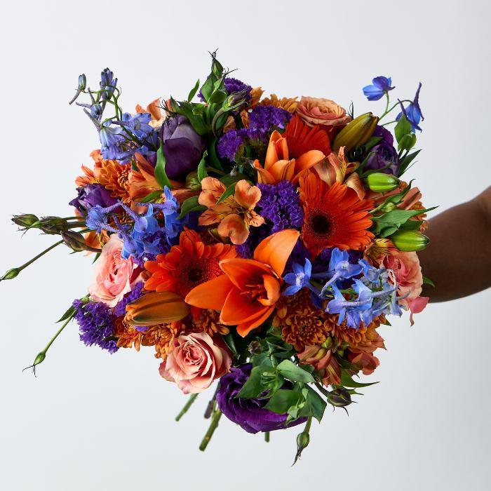Colourful array of women's flower bouquet gift with orange lilies, purple lisianthis, statice and blue delphinium - Flower Guy