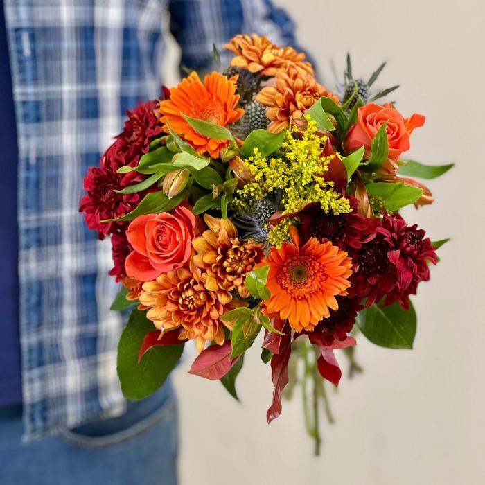 Close-up view of Flower Guy's red chrysanthemum bouquet with orange gerberas, orange roses, red and orange chrysanthemums, golden rod, sea holly, and a lush assortment of greenery - Flower Guy
