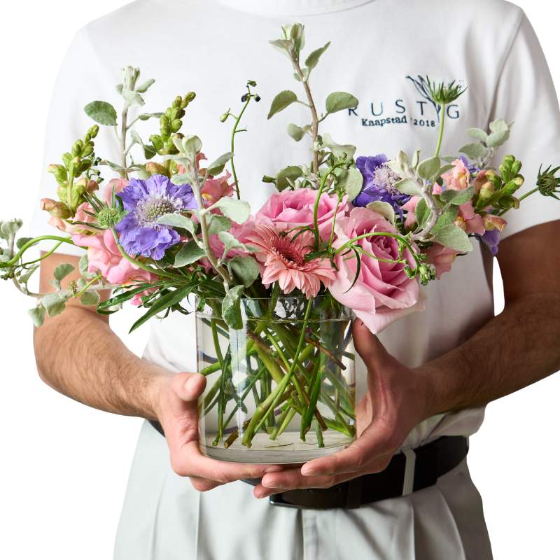 Pastel Dream flower arrangement in clear glass vase—pastel pink and lavender blooms with greenery, held in hands | Flower Guy