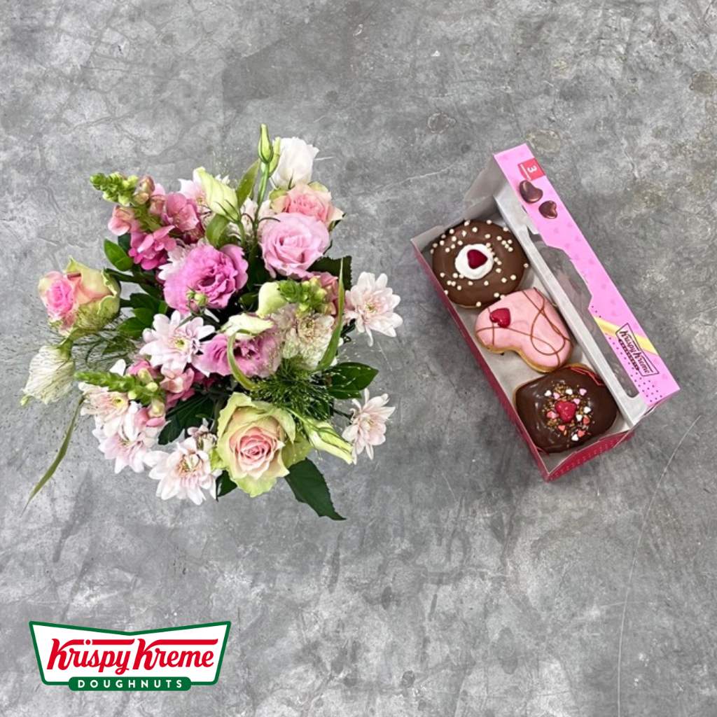 Assorted Krispy Kreme doughnuts alongside a vibrant floral arrangement - Petals & Pastries Deluxe Duo by Flower Guy.