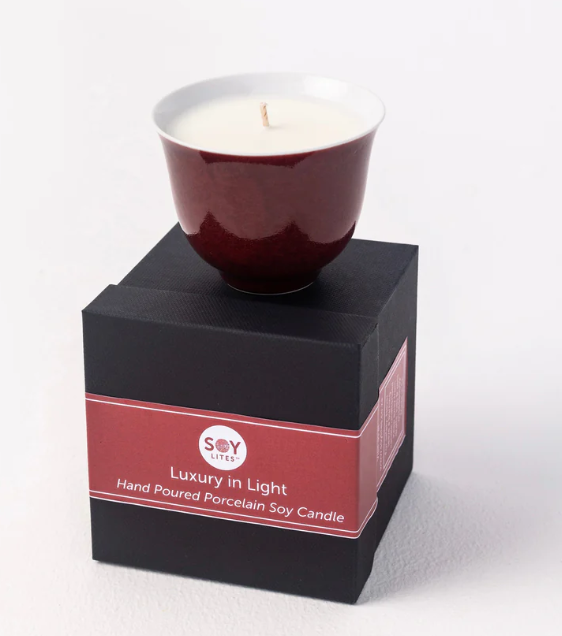 Red candle in a white container on a black box with 'Soy Candles' branding.