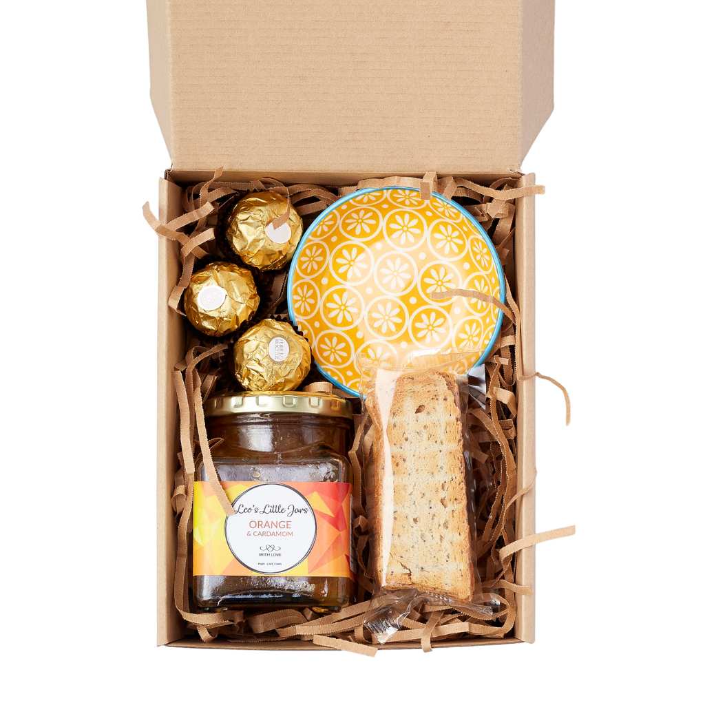 Sunshine in a Gift Box—open gift box with orange marmalade jar, Ferrero Rocher chocolates, biscotti and a yellow ceramic bowl | Flower Guy