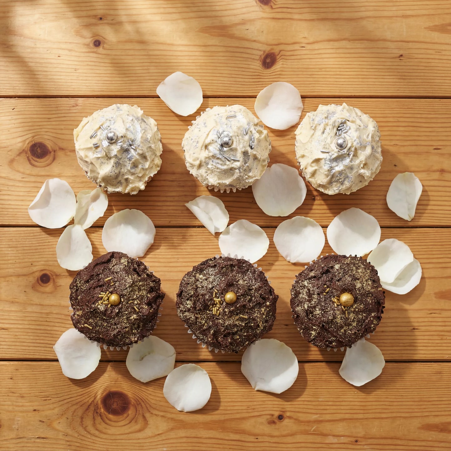 Overhead flat lay of Where Frosting Meets Fate vanilla and chocolate cupcakes with scattered white rose petals