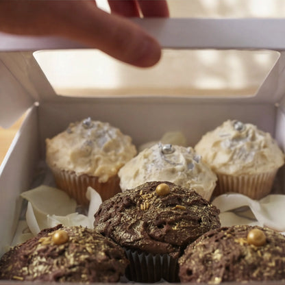 Hand lifting lid on Where Frosting Meets Fate cupcake box revealing gold chocolate and silver vanilla cupcakes