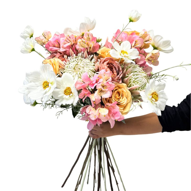 Bouquet of pink, white, and yellow flowers held by a person against a white background